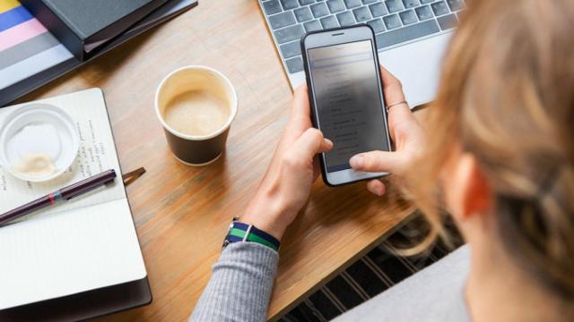 Una mujer consultando los mensajes de su móvil en horas de trabajo