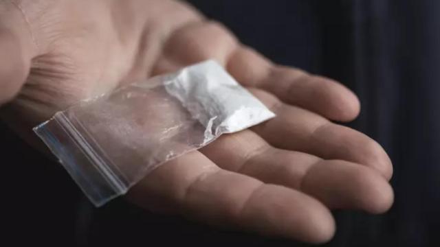 Mano de hombre sosteniendo un paquete de plástico con polvo de Tina u otra sustancia / DEDMITYAY - ISTOCK