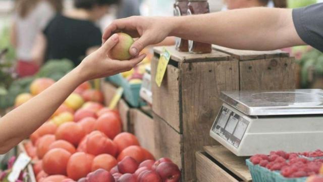 Uno de los comerciantes barceloneses entrega una pieza de fruta a un cliente en una imagen de archivo / EP