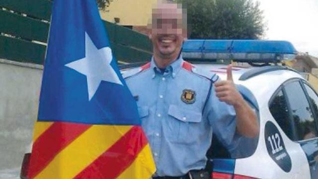 Un mosso d'Esquadra uniformado posa con la bandera independentista ante su coche patrulla / CG