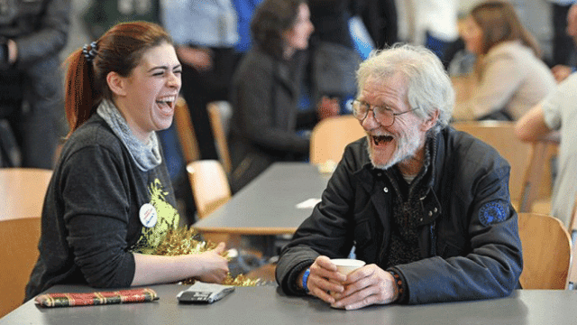 Una voluntaria ríe junto a un vagabundo en un centro social / PA