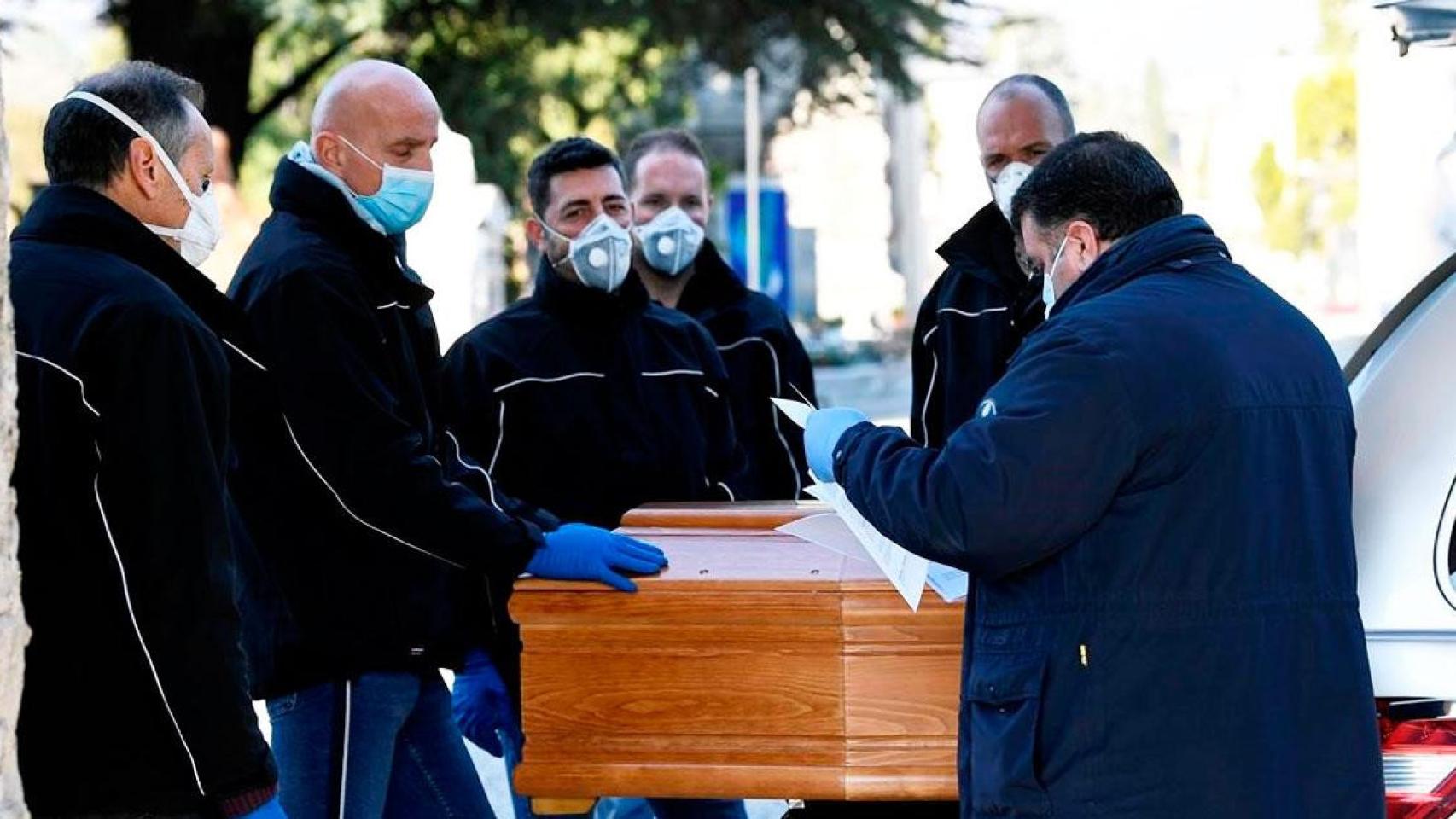 Imagen de operarios con mascarilla de una funeraria de Madrid trasladando un féretro / EFE