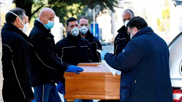 Imagen de operarios con mascarilla de una funeraria de Madrid trasladando un féretro / EFE