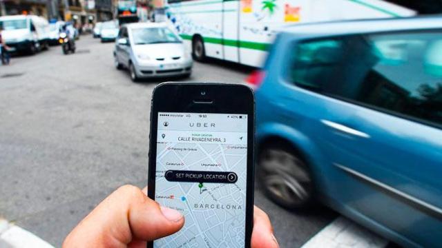 Imagen de la aplicación de servicios VTC Uber con tráfico en una calle de Barcelona de fondo / CG