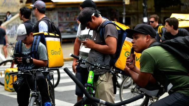 Varios repartidores de Glovo consultando su móvil