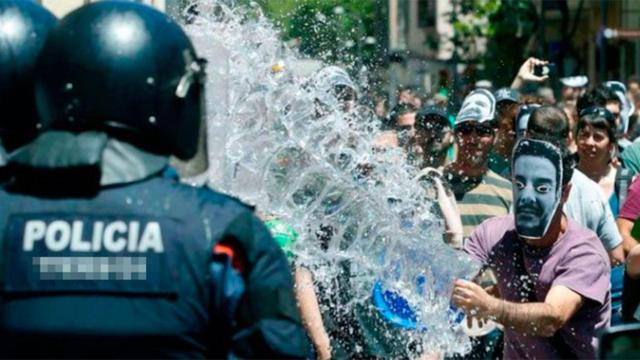 Uno de los okupas del Banc Expropiat de Gràcia lanza un cubo de agua a una de sus víctimas, un agente de los Mossos. La asociación de víctimas de okupas llega a Cataluña / EFE
