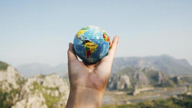 Viajero sosteniendo en su mano un globo terráqueo, cómo viajan los más y menos ricos / PEXELS