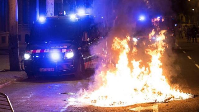 Una furgoneta de los Mossos d'Esquadra pasa junto a la hoguera hecha por los manifestantes / EFE