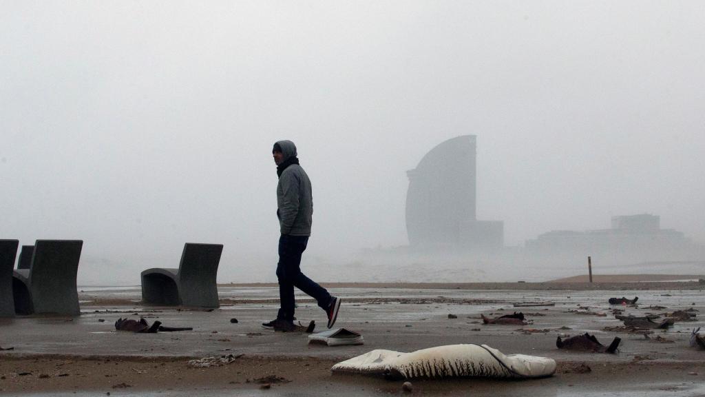 Una persona pasea por la playa con el viento de cara durante el temporal Gloria que ha azotado Barcelona
