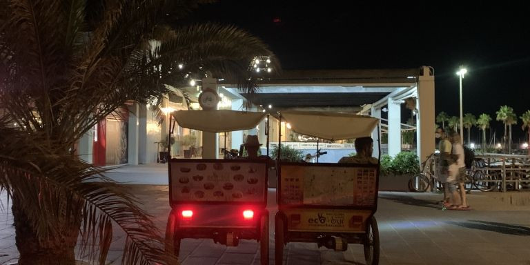 Dos bicitaxis esperando para captar clientes en el paso elevado del Port Olímpic / METRÓPOLI ABIERTA