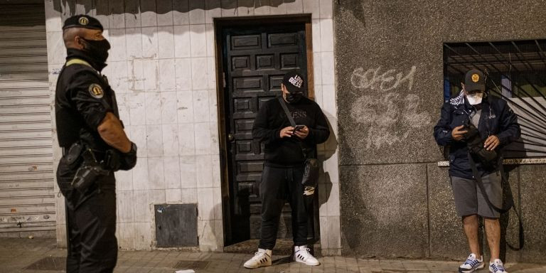 Un agente de la Omega vigila a dos hombres que incumplían el toque de queda nocturno mientras son idenfiticados / PABLO MIRANZO