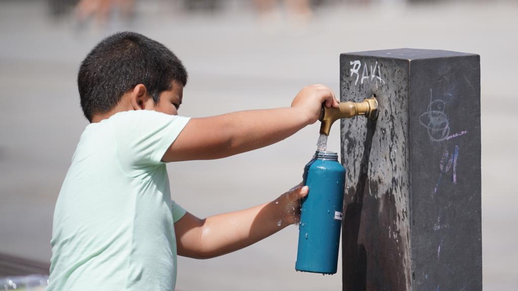 Un niño se aprovisiona de agua en una fuente en plena ola de calor