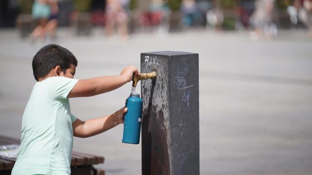 Un niño se aprovisiona de agua en una fuente en plena ola de calor