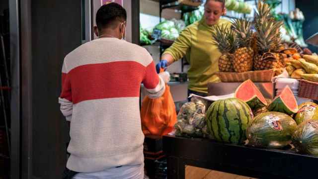 Uno de los repartidores del servicio a domicilio del Mercado de Sant Antoni recoge un pedido en un puesto de frutas y verduras