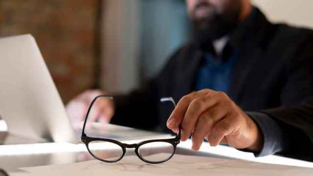 Un hombre frente a su portátil coge unas gafas