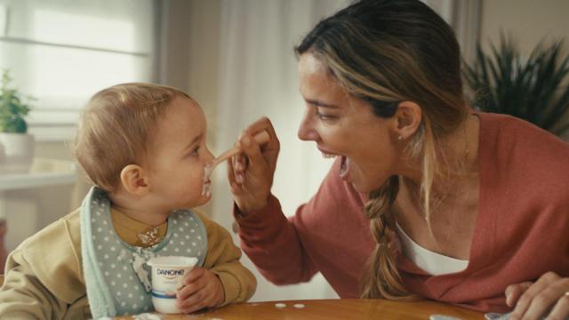 Una madre da de comer a un niño un yogurt Danone