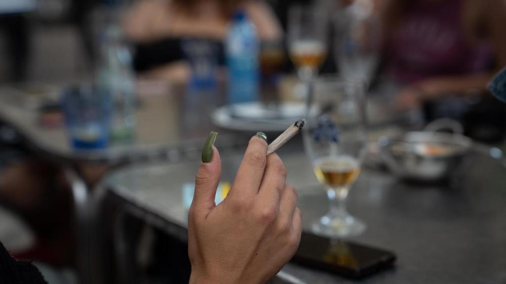Una dona fuma asseguda a la taula d'una terrassa