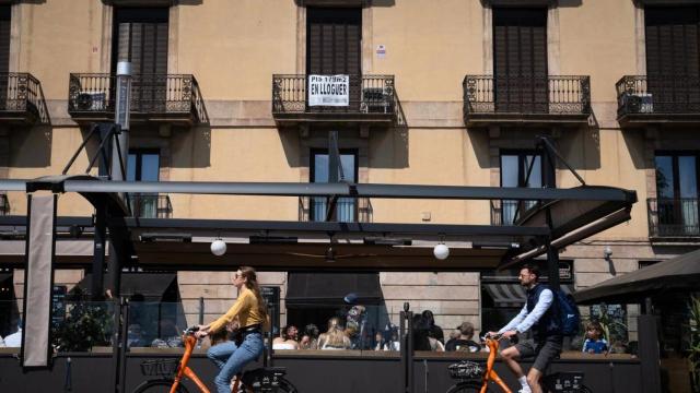Dos vecinos, circulando en bicicleta ante un piso en alquiler en Barcelona