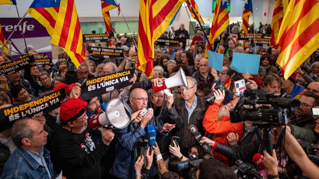 El presidente de la ANC, Lluís Llach (c), atiende a los medios de comunicación durante una concentración por las incidencias en Rodalies, en la estación de Sants