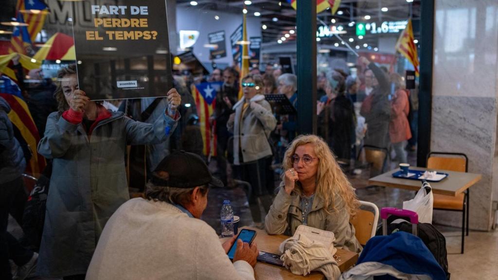 Dos clientes de una cafetería de la estación de Sants, con la manifestación independentista de la ANC de fondo