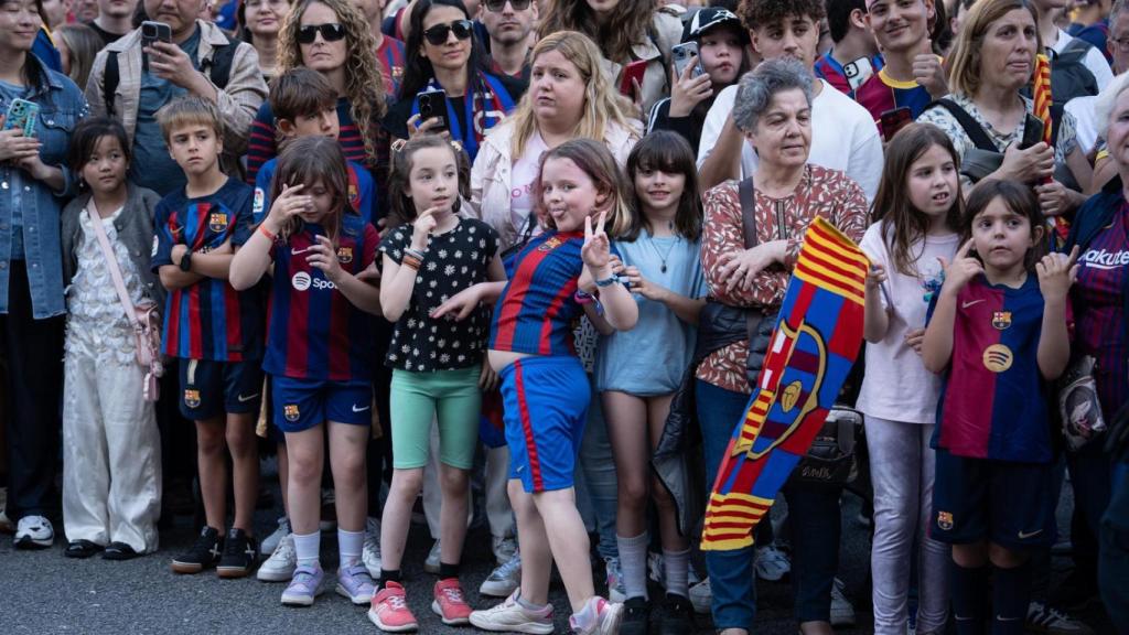 Las familias de culés aguardan el paso de sus ídolos en la rúa del Barça