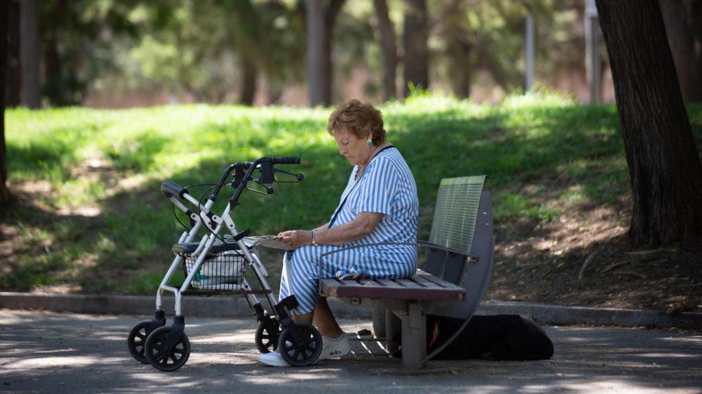 Una mujer lee bajo la sombra de unos árboles en el parque de la Barceloneta