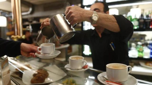 Un trabajador sirve cafés en un local de hostelería pequeño y de barrio