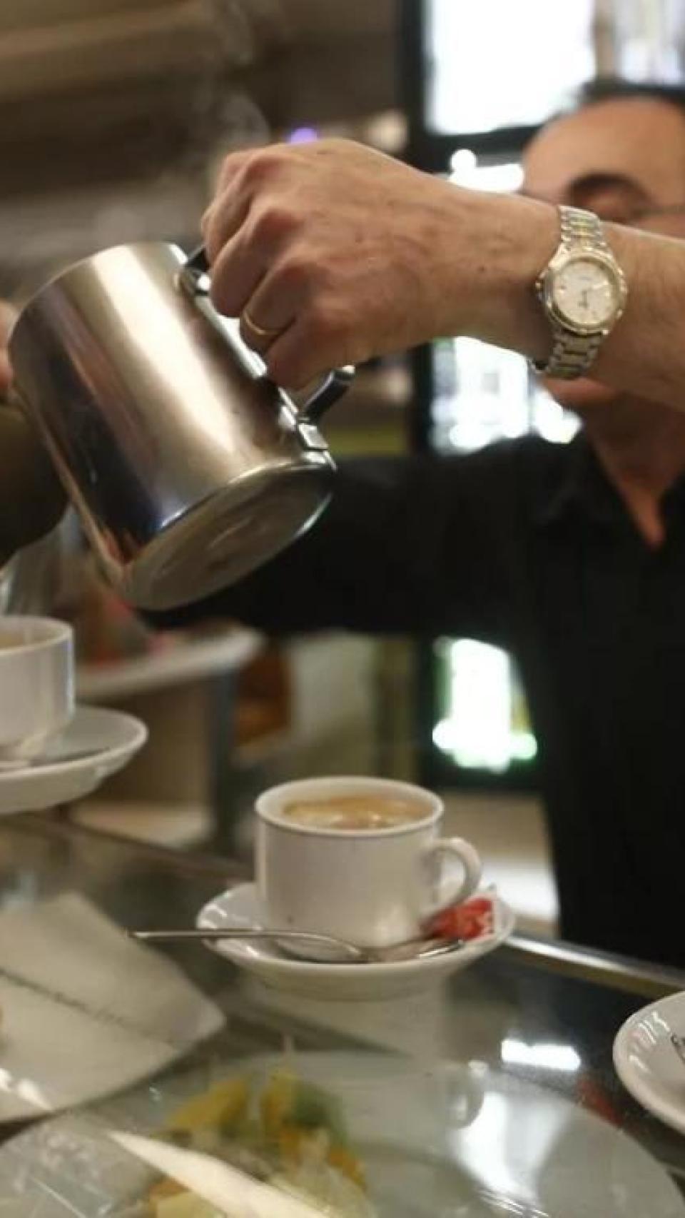 Un treballador serveix cafès en un local d’hostaleria petit i de barri