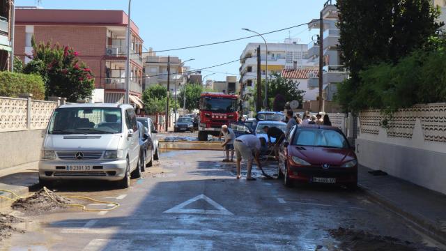 Varias personas limpian barro de una calle en Cubelles, mientras los bomberos buscan a las desaparecidas