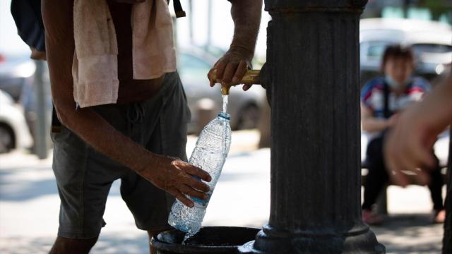 Una persona llena una botella de agua en una fuente de Barcelona en plena ola de calor