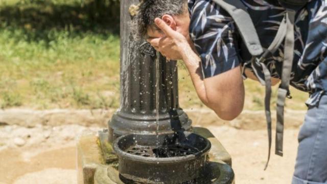 Un hombre se refresca en una fuente en un día de verano