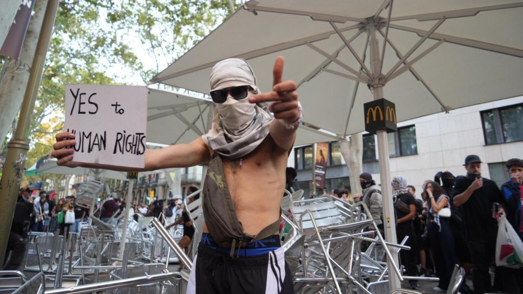 Un manifestante anónimo muestra un cartel de Sí a los Derechos Humanos, frente a la montaña de mesas y sillas en la terraza del Mc Donald's