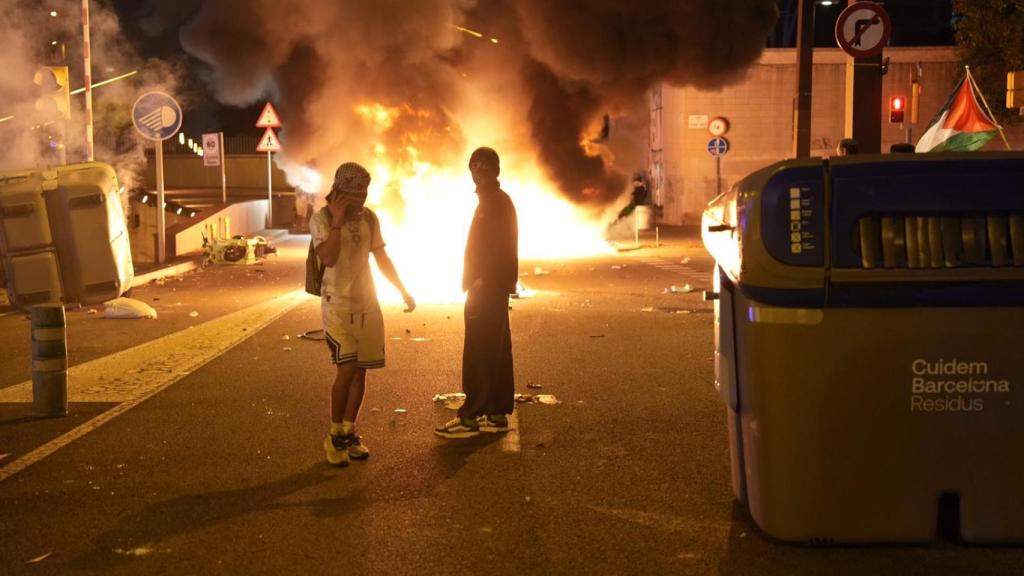 Dos jóvenes posan ante contenedores en llamas durante la huelga general propalestina en Barcelona