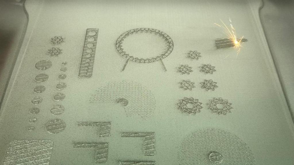 Proceso de fabricación de las piezas, donde se observan varias de ellas y un láser consolidando una sobre el lecho de polvo