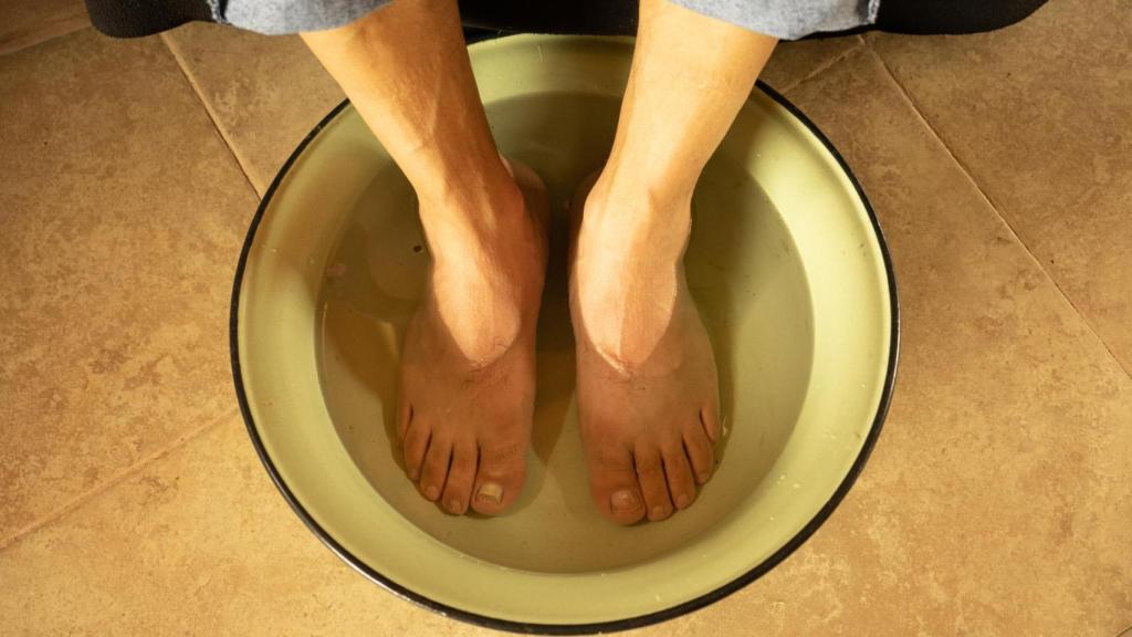 Hombre con los pies dentro de un cubo de agua