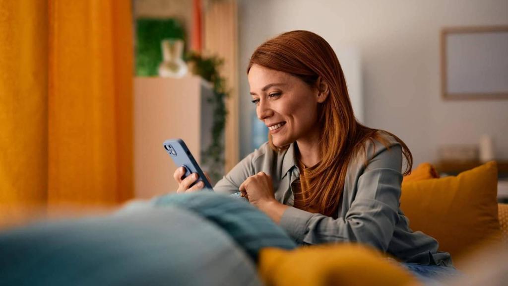 Mujer sonríe con su móvil en la mano