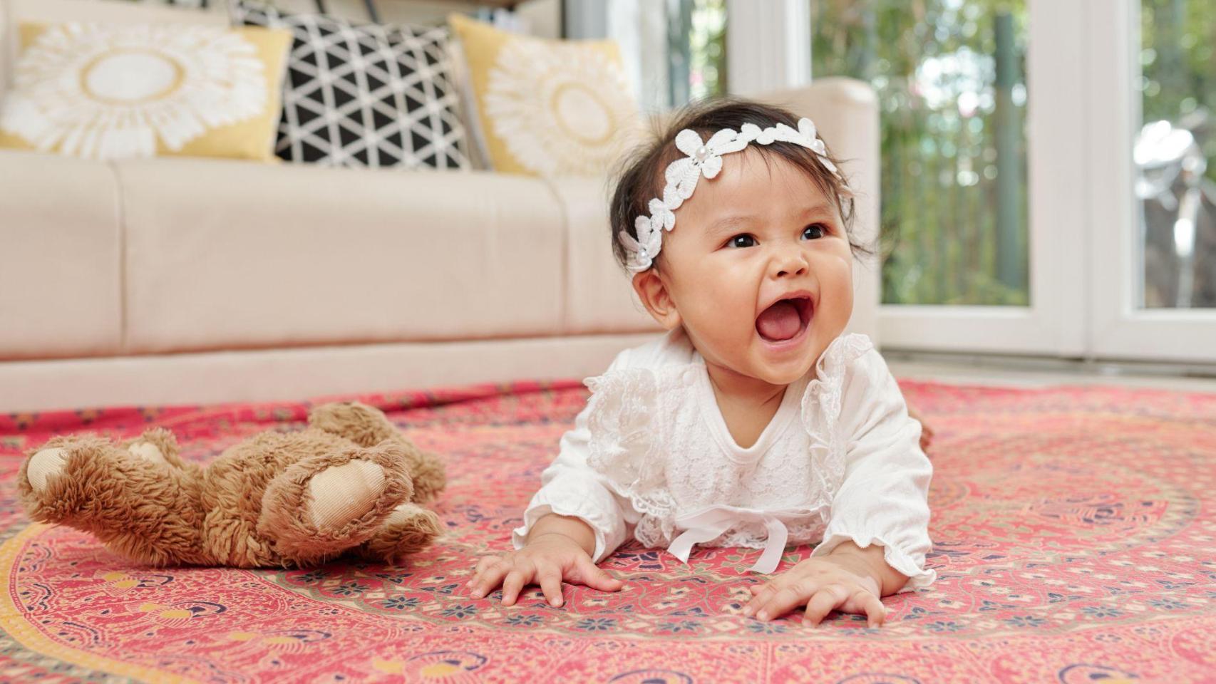 Una niña gatea en el suelo al lado de un juguete