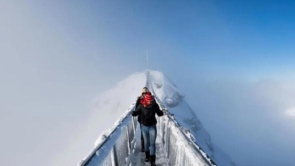 Dos turistas caminan sobre un puente colgante en el paso de montaña Col du Pillon, entre Gstaad y Les Diablerets (Suiza).