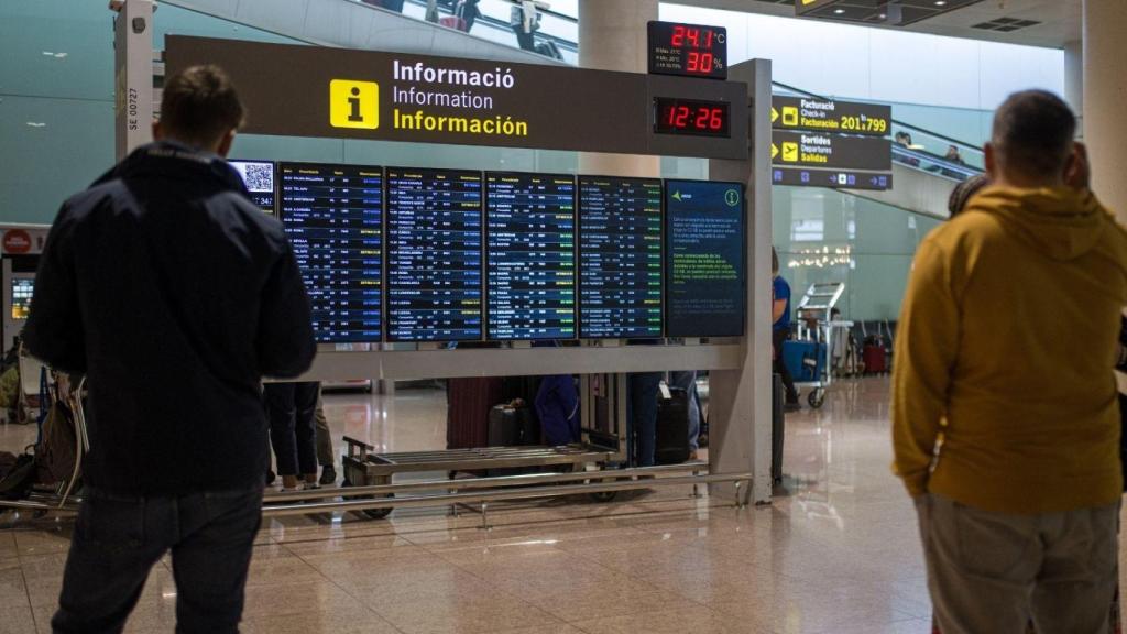 Varias personas observan un panel de llegadas en el aeropuerto de Barcelona-El Prat