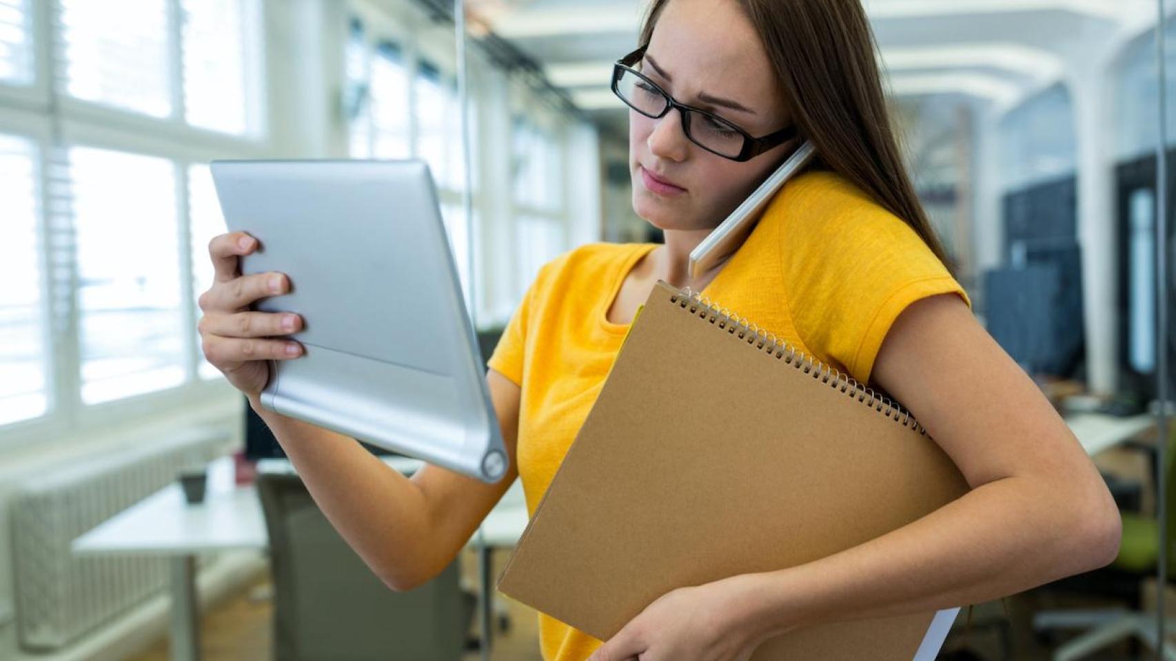 Mujer consulta su tablet mientras habla y sujeta una carpeta