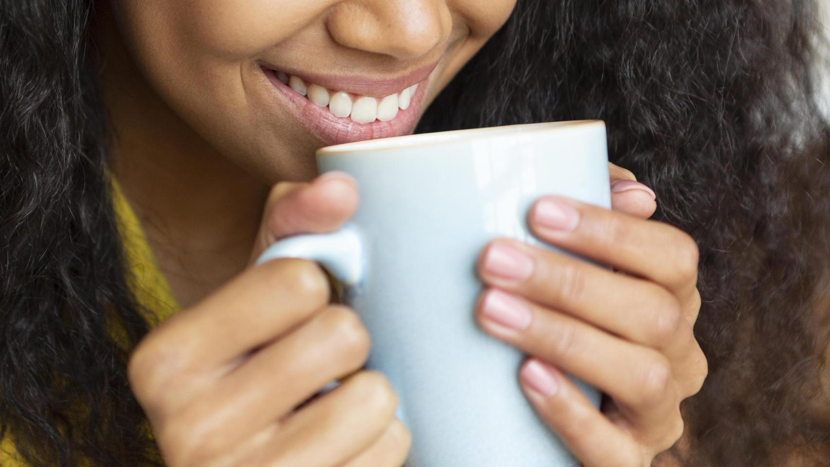 Mujer sonríe mientras toma una taza de café