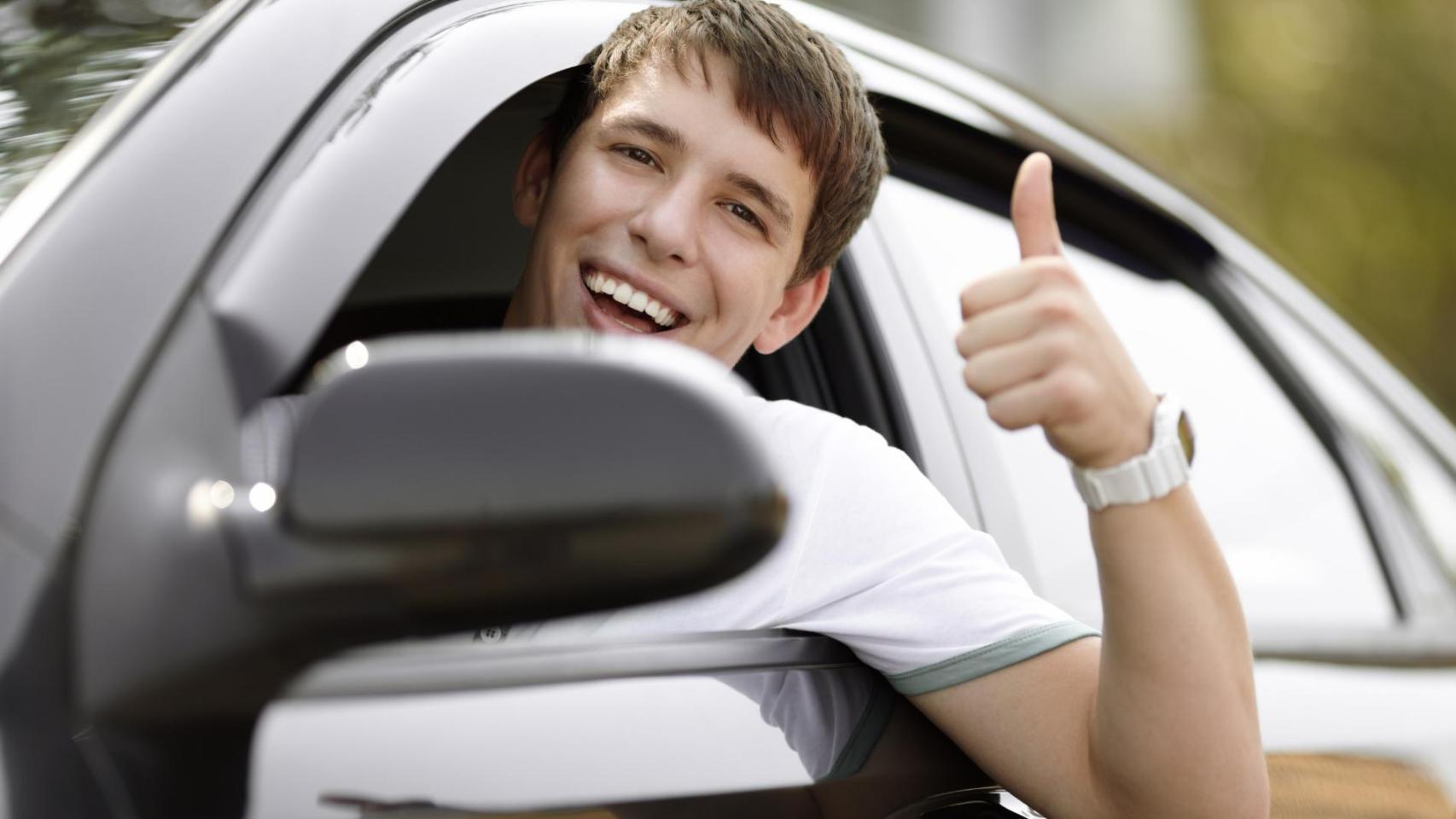 Joven sonriente dentro de un coche haciendo gesto de aprobación, representando a menores que obtienen el carnet de conducir