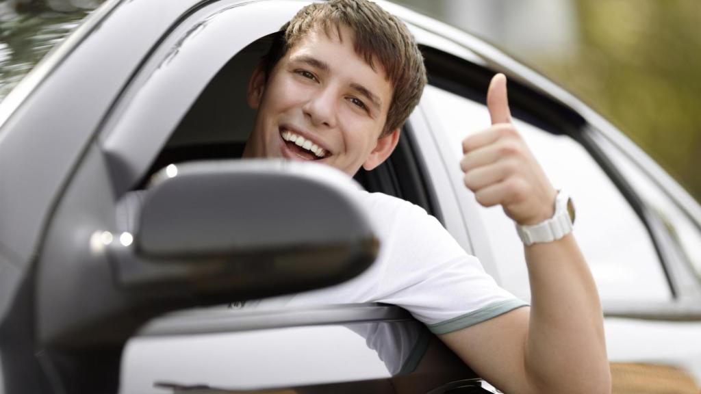 Joven sonriente dentro de un coche haciendo gesto de aprobación, representando a menores que obtienen el carnet de conducir