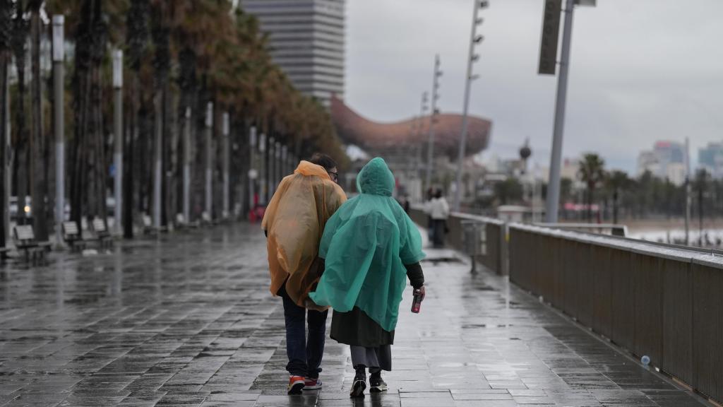 Vecinos de Barcelona pasean bajo la lluvia en la playa de la Barceloneta, en enero