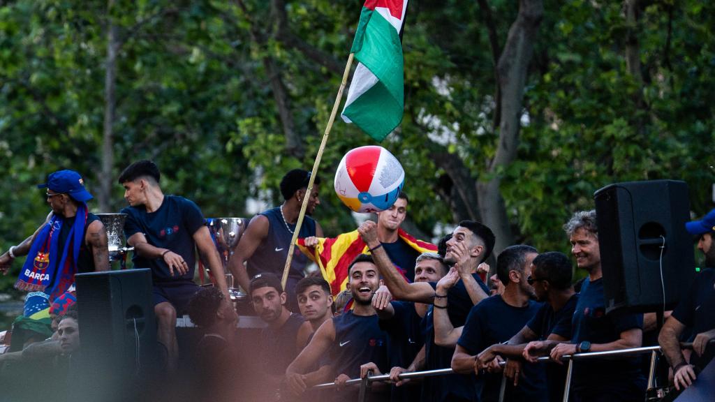 Los jugadores del Barça, con un balón de playa y una bandera de Palestina en la rúa de campeones