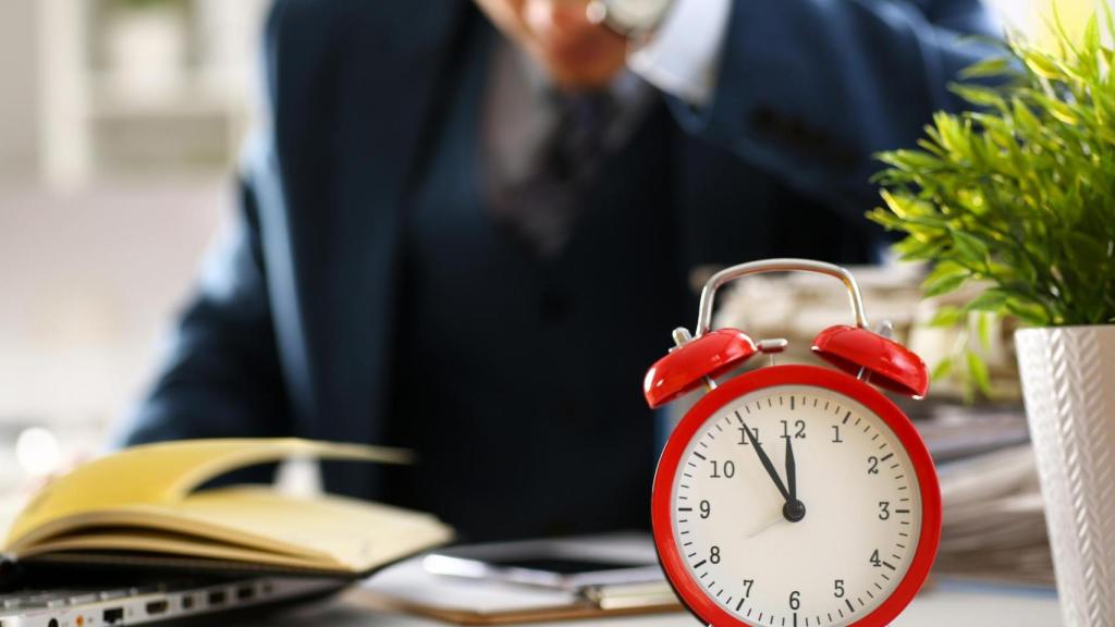 Trabajador preocupado por llegar tarde junto a un reloj sobre el escritorio