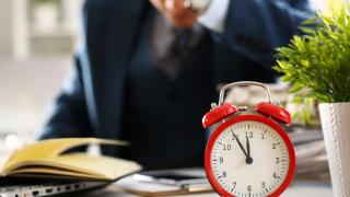 Trabajador preocupado por llegar tarde junto a un reloj sobre el escritorio