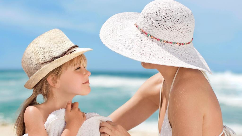 Una mujer y una niña con sombrero en la playa. En verano, la piel está más expuesta a los efectos nocivos de la radiación solar