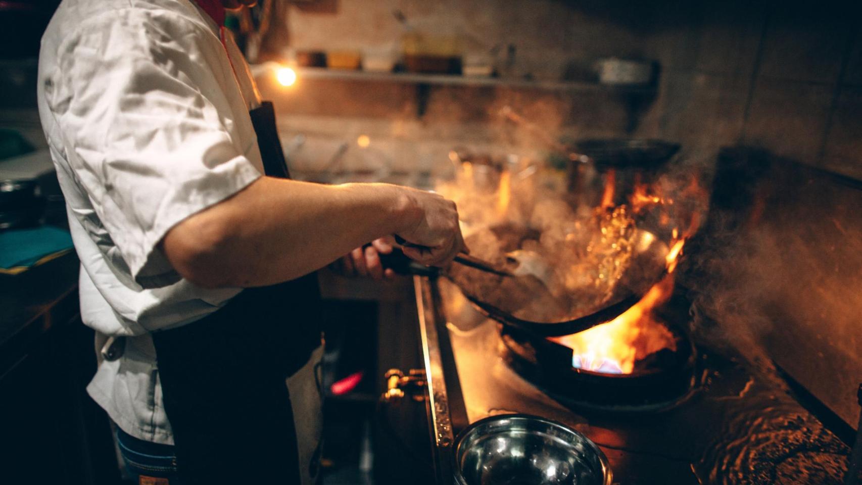Cocinero trabajando entre humo y fuego en un restaurante, afectado por la nueva normativa de ventilación y extracción en España