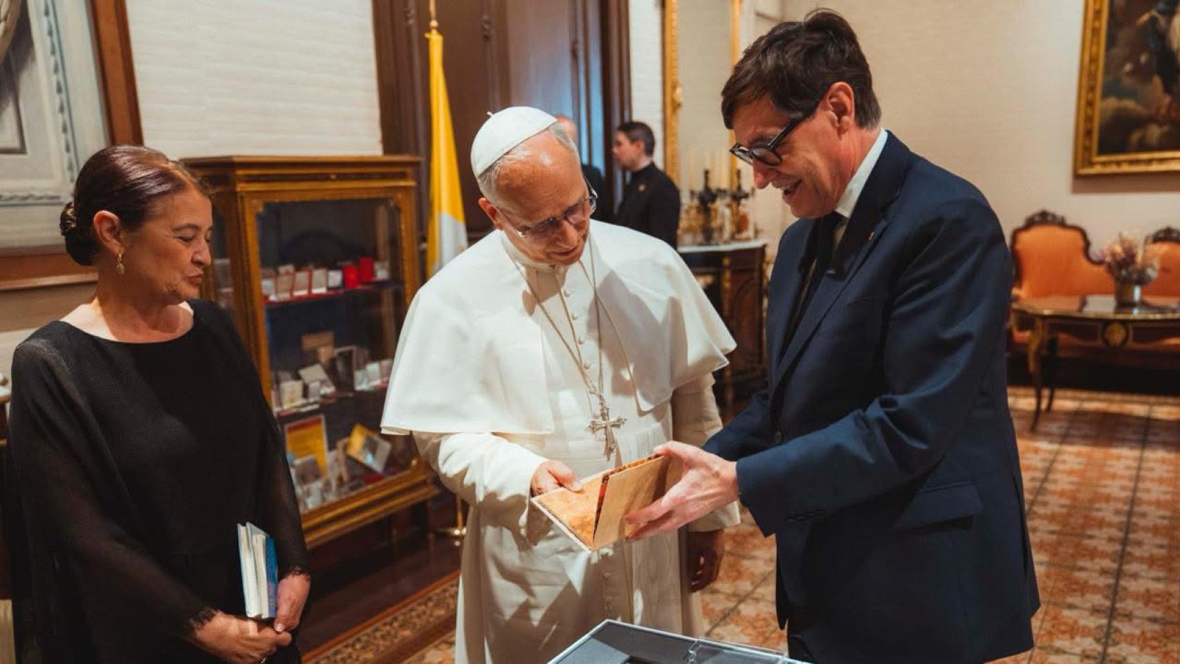 El presidente de la Generalitat, Salvador Illa, entrega un obsequio al Papa León XIV en el Palau Episcopal de Barcelona, acompañados por la mujer del dirigente catalán, Marta Estruch, a 9 de junio de 2026